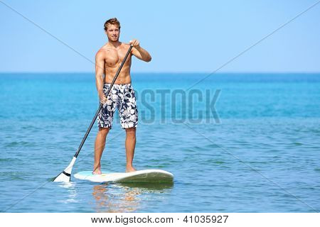 Picture or Photo of Stand up paddle board man paddleboarding on Hawaii standing happy on paddleboard on blue water. Young caucasian male model on Hawaiian beach on summer holidays vacation travel.