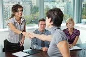 picture of handshake  - Panel of business people sitting at table in meeting room conducting job interview greeting female applicant - JPG 
