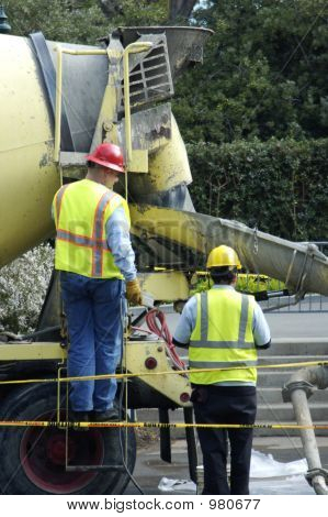 Picture or Photo of Two construction workers fixing the road wearing yellow and red hard hats and yellow safety wear.