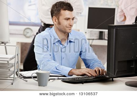 Picture or Photo of Casual businessman working in office, sitting at desk, typing on keyboard, looking at computer screen.?