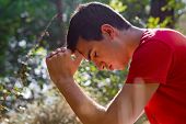 stock photo of religion  - Young man kneeling and praying in forest - JPG 