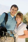stock photo of golf  - Portrait of a happy couple carrying golf bag on golf course - JPG 