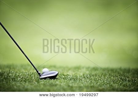 Picture or Photo of Golf ball behind driver at driving range, plenty of copy-space and very shallow depth of field.