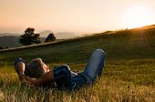 foto of sunset  - Mature man taking a break and relax in a meadow in the wonderful warm light of the sunset - JPG 