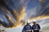 foto of industrial  - two engineers walking under a symbolic industrial sunset cloud and sky - JPG 
