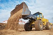 foto of construction worker  - Wheel loader machine unloading sand at eathmoving works in construction site - JPG 