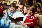 stock photo of reading  - Portrait of friendly family reading book on Christmas evening - JPG 