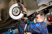 stock photo of industrial  - car mechanic examining car suspension of lifted automobile at repair service station - JPG 