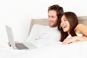 stock photo of home  - Happy couple with laptop in bed watching fun movie on computer in bed before sleeping - JPG 