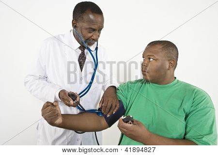 Picture or Photo of An African American doctor looking at obese patient while checking blood pressure in clinic