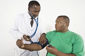 stock photo of pressure  - An African American doctor looking at obese patient while checking blood pressure in clinic - JPG 
