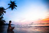 image of sunset  - Beautiful woman doing lotus yoga pose on the beach near the ocean at sunset in Thailand - JPG 