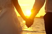 stock photo of holding  - Young adult male groom and female bride holding hands on beach at sunset - JPG 