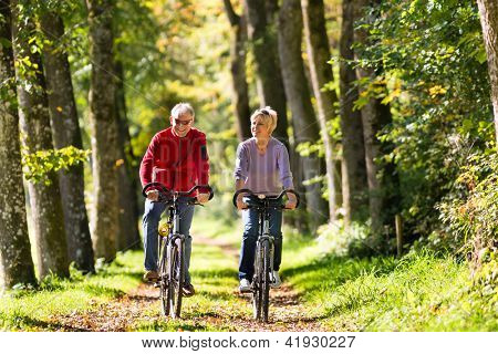 Picture or Photo of Senior Man and woman exercising with bicycles outdoors, they are a couple