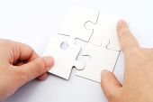 stock photo of puzzle  - Hand holding puzzle piece and inserting it into group of white paper jigsaw puzzles - JPG 