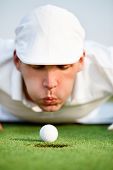 picture of golf  - Desperate golfer blowing on golf ball to put in hole - JPG 